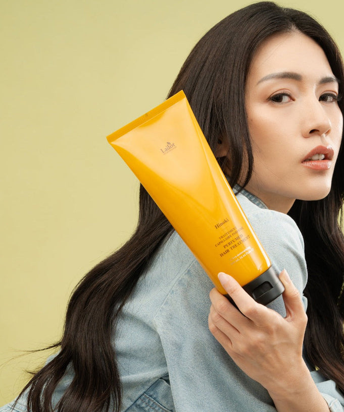 Woman holding LADOR Perfume Hair Treatment 380ml against light green background