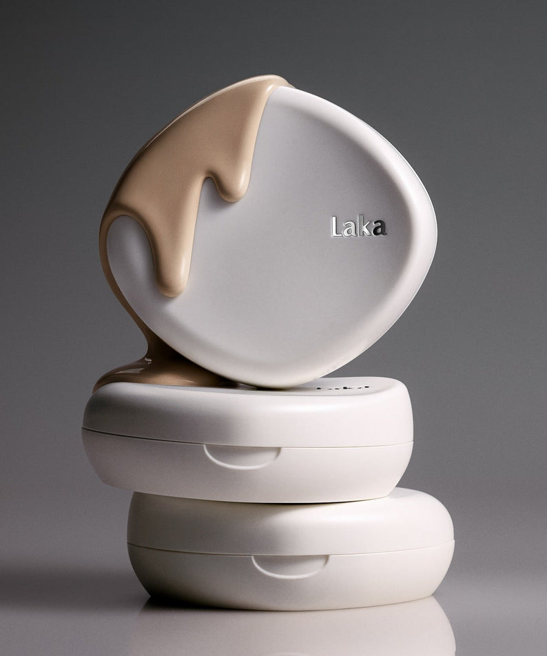 Stack of LAKA Bonding Cover Cushion compacts with beige cream flowing over the top, highlighting the LAKA Bonding Cover Cushion product.
