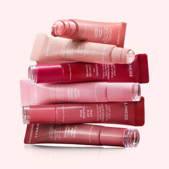 Assorted shades of LANEIGE Glaze Craze Tinted Lip Serum tubes arranged on a soft pink background