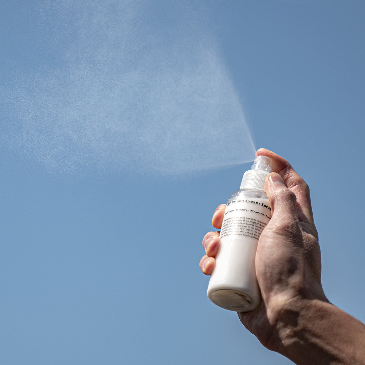 LAZY SOCIETY All-in-One Cream Spray 120ml being sprayed by a man’s hand against blue sky – Gentleman Korea Korean men’s skincare
