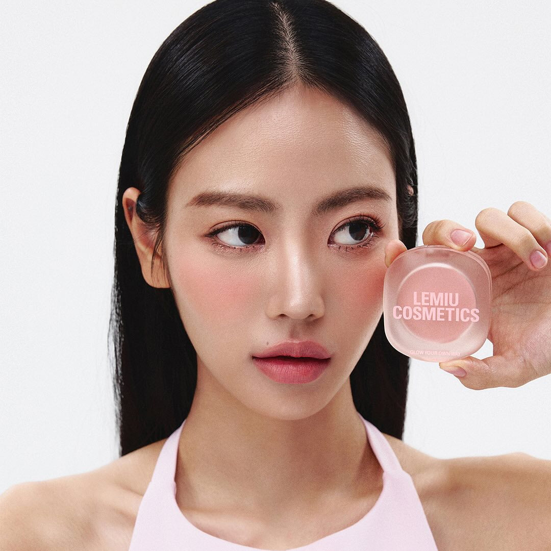 Woman holding LEMIU Eye To Cheek product near her face, showcasing its use for eye and cheek beauty.