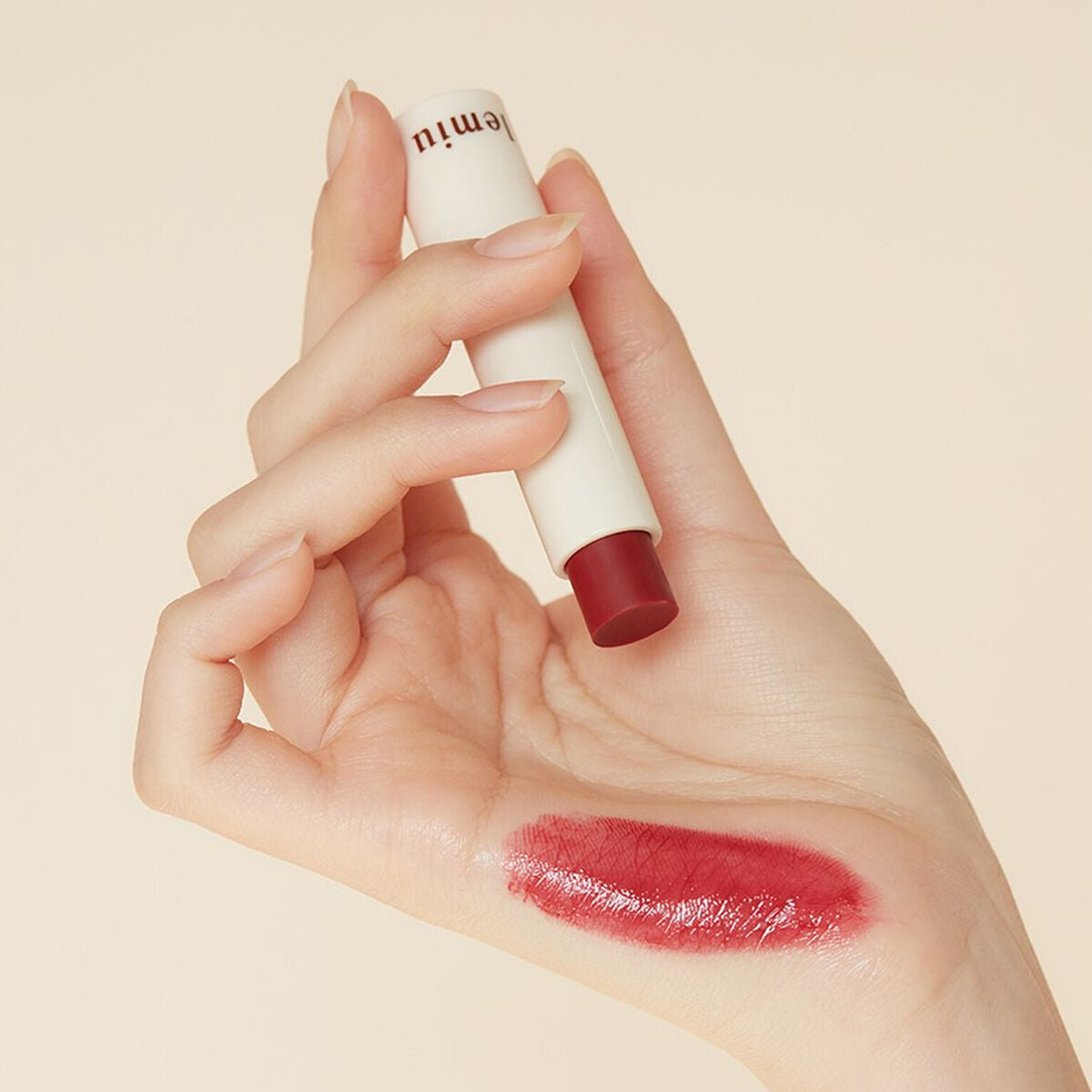 Hand holding LEMIU Sole Mood Vegan Lip Balm with swatch on skin.