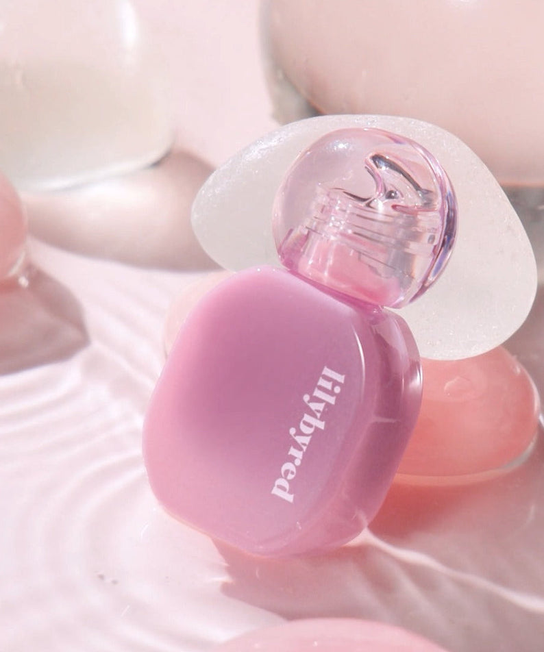 LILYBYRED Balming Dewy Tint in a pink hue with a stylish transparent cap placed on a reflective surface.