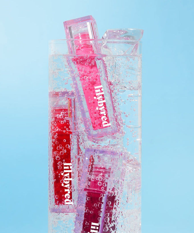 LILYBYRED Juicy Liar Water Tint bottles submerged in a glass of sparkling water against a blue background.
