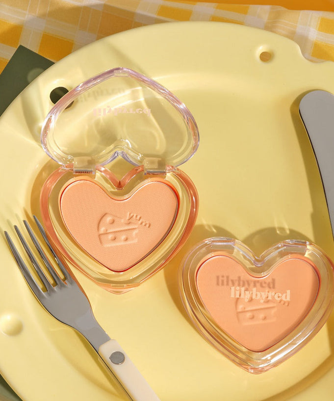 LILYBYRED Luv Beam Blur Cheek #CheeseEdition heart-shaped blush compact on a yellow plate with fork and knife.