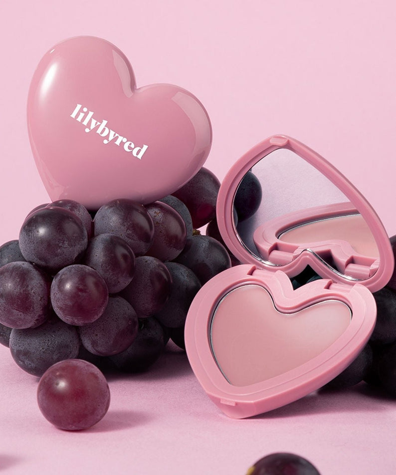LILYBYRED Love Beam Cheek Balm in heart-shaped compact with grapes on a pink background
