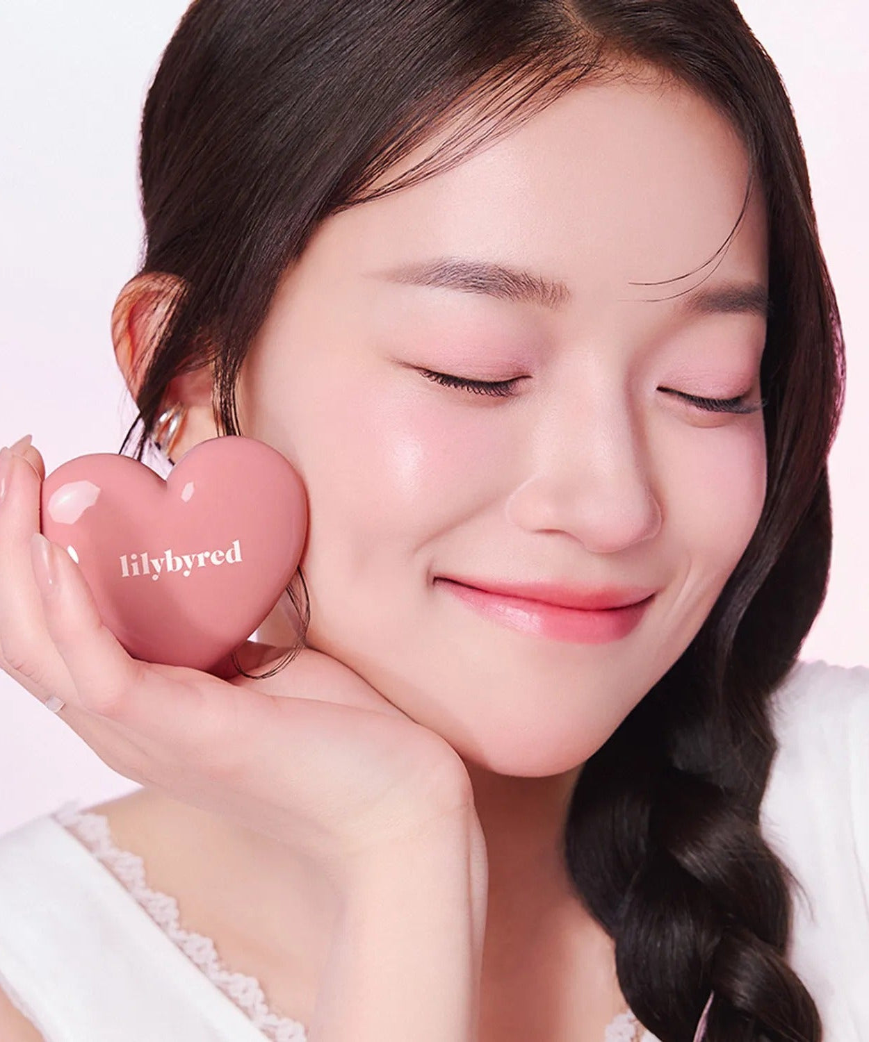 Woman holding LILYBYRED Love Beam Cheek Balm in heart-shaped container, showing natural glow and blush.