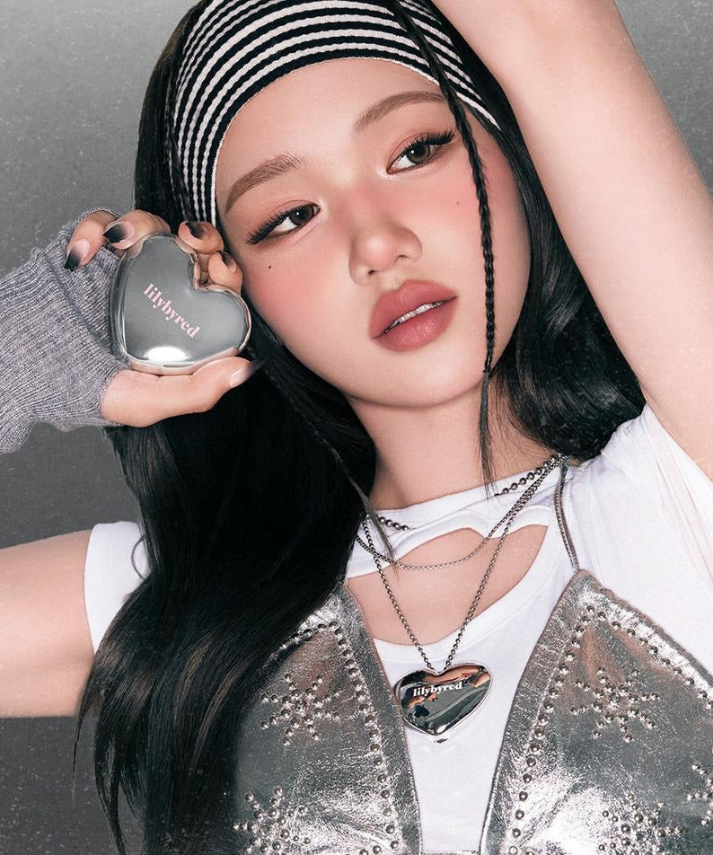 Person holding a heart-shaped container of LILYBYRED Love Beam Cheek Mousse with a reflective surface. Product packaging close-up.