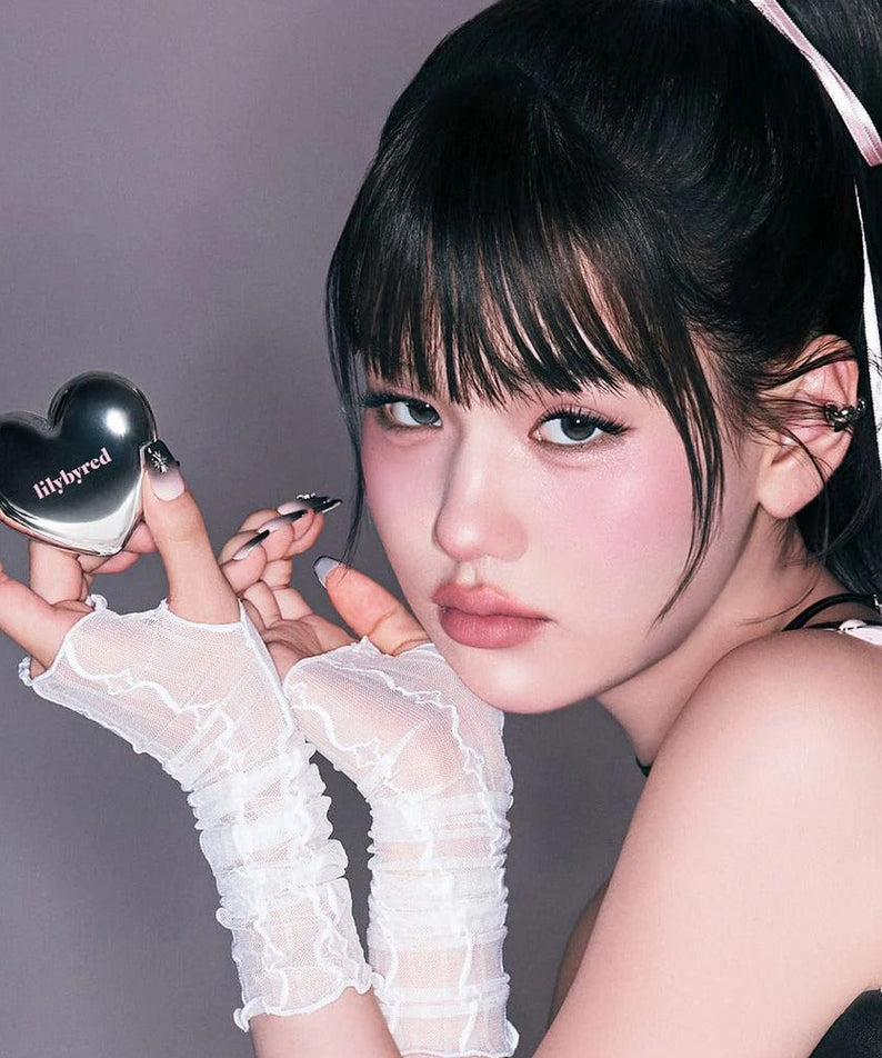 Model holding heart-shaped LILYBYRED Love Beam Cheek Mousse, showing blush effect on cheeks.