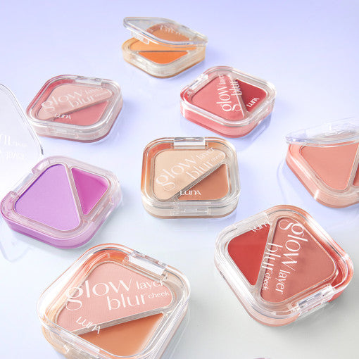 Various shades of LUNA Glow Layer Blur Cheek compacts arranged aesthetically on a light purple background.