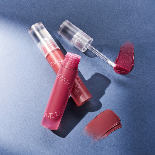 LUNA Over Blur Fixing Tint in red and mauve shades with applicator on a blue surface.