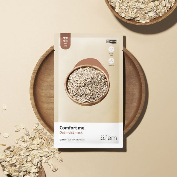 MAKE P:REM Comfort Me Oat Moist Mask packaging with oats on a wooden background, showcasing a vegan skincare product.