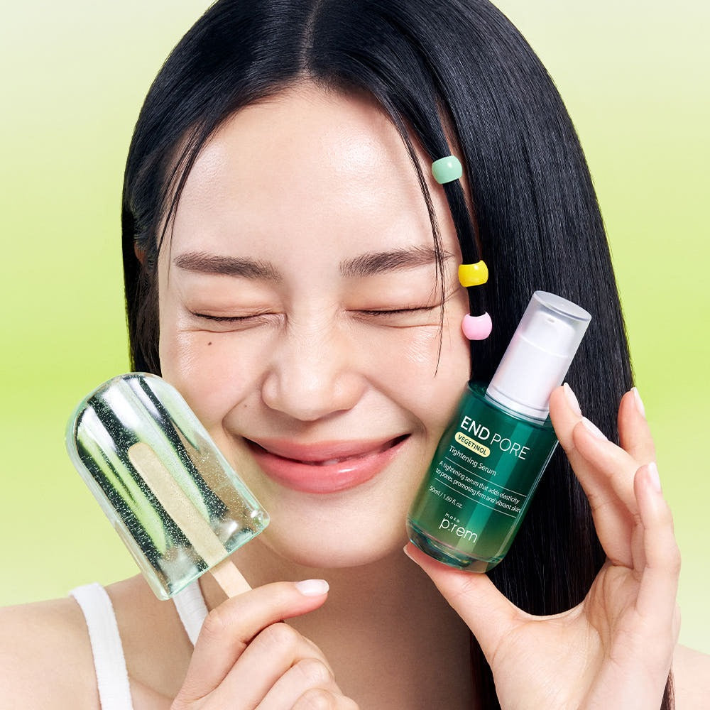 Smiling woman holding MAKE P:REM Endpore Vegetinol Tightening Serum 50ml with a dropper on green background