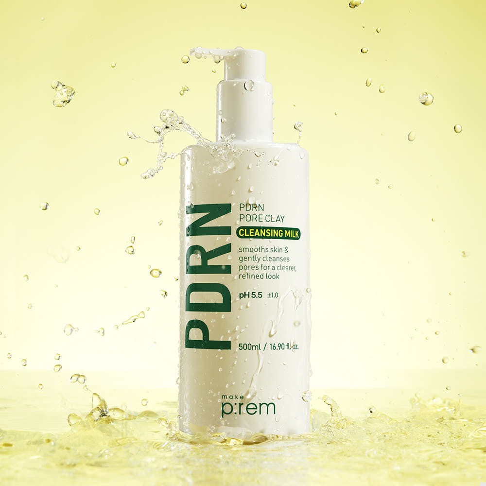 Bottle of MAKE P:REM PDRN Pore Clay Cleansing Milk 500ml with water splashes on yellow background