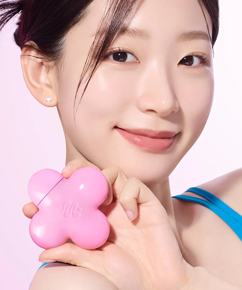 Person holding a pink flower-shaped beauty product case, smiling, with a clear complexion and wearing a blue top.