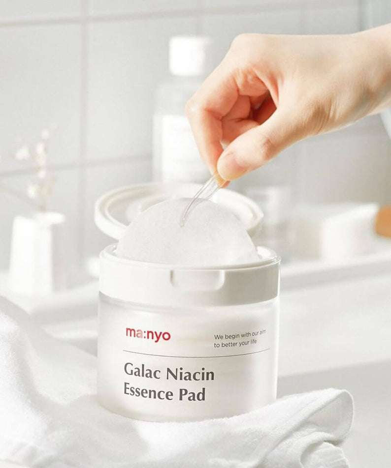 MANYO Galac Niacin Essence Pad 80 Sheets in a bathroom setting, showcasing a hand using the skincare product for facial care.