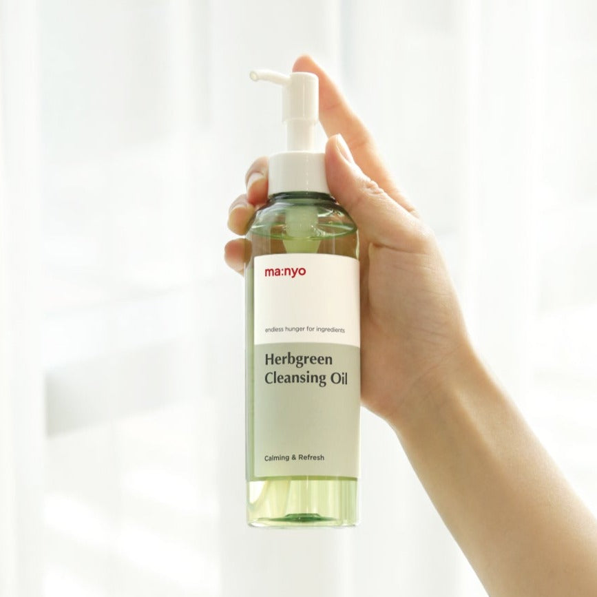 Hand holding MA:NYO Herbgreen Cleansing Oil 200ml bottle against a light background.