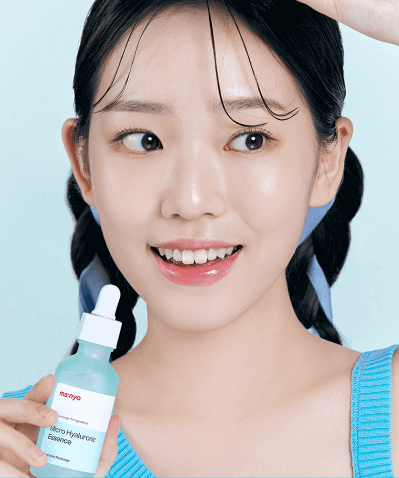 Person holding MANYO Micro Hyaluronic Essence 50ml bottle, smiling, on a blue background.
