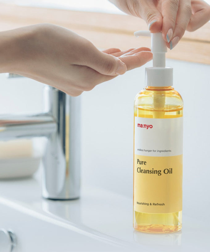 Person using MA:NYO Pure Cleansing Oil bottle at a sink, showcasing skincare product.