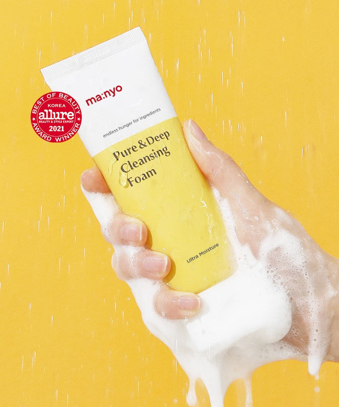 Hand holding MA:NYO Pure & Deep Cleansing Foam 200ml with foam against a yellow background, highlighting skincare product packaging.