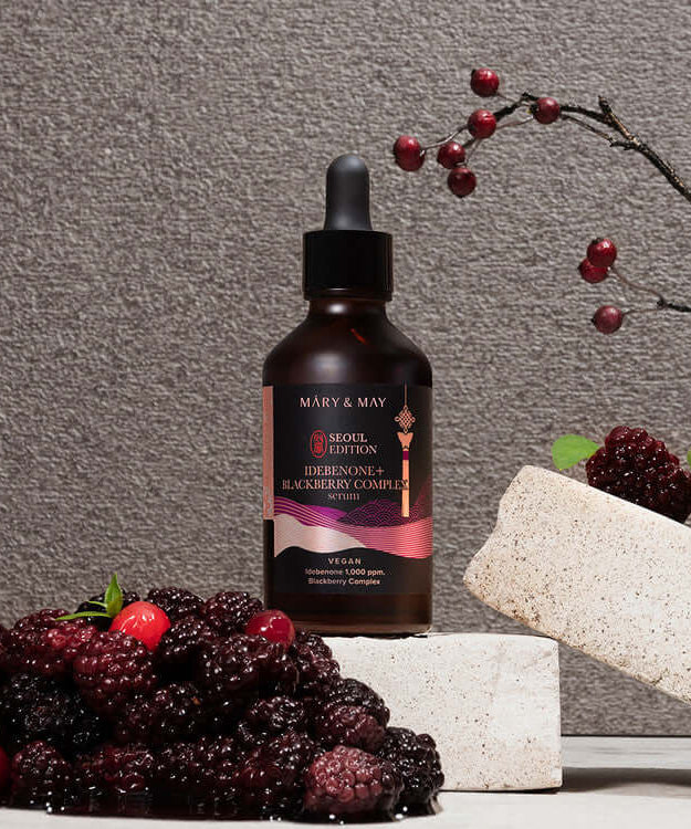 MARY & MAY Idebenone+Blackberry Complex Serum bottle with fresh blackberries on a stone display