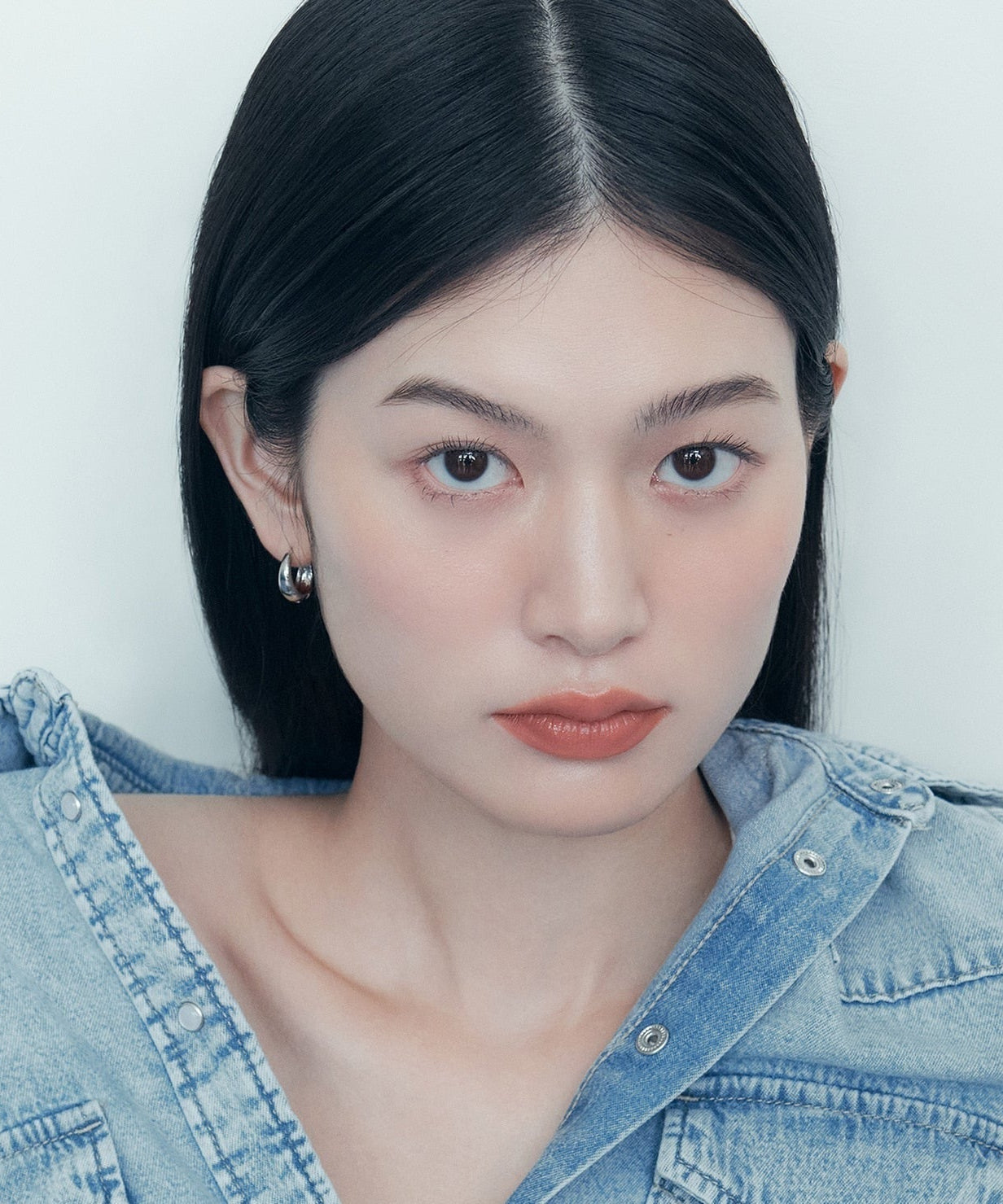 A person with long black hair wearing a denim jacket.