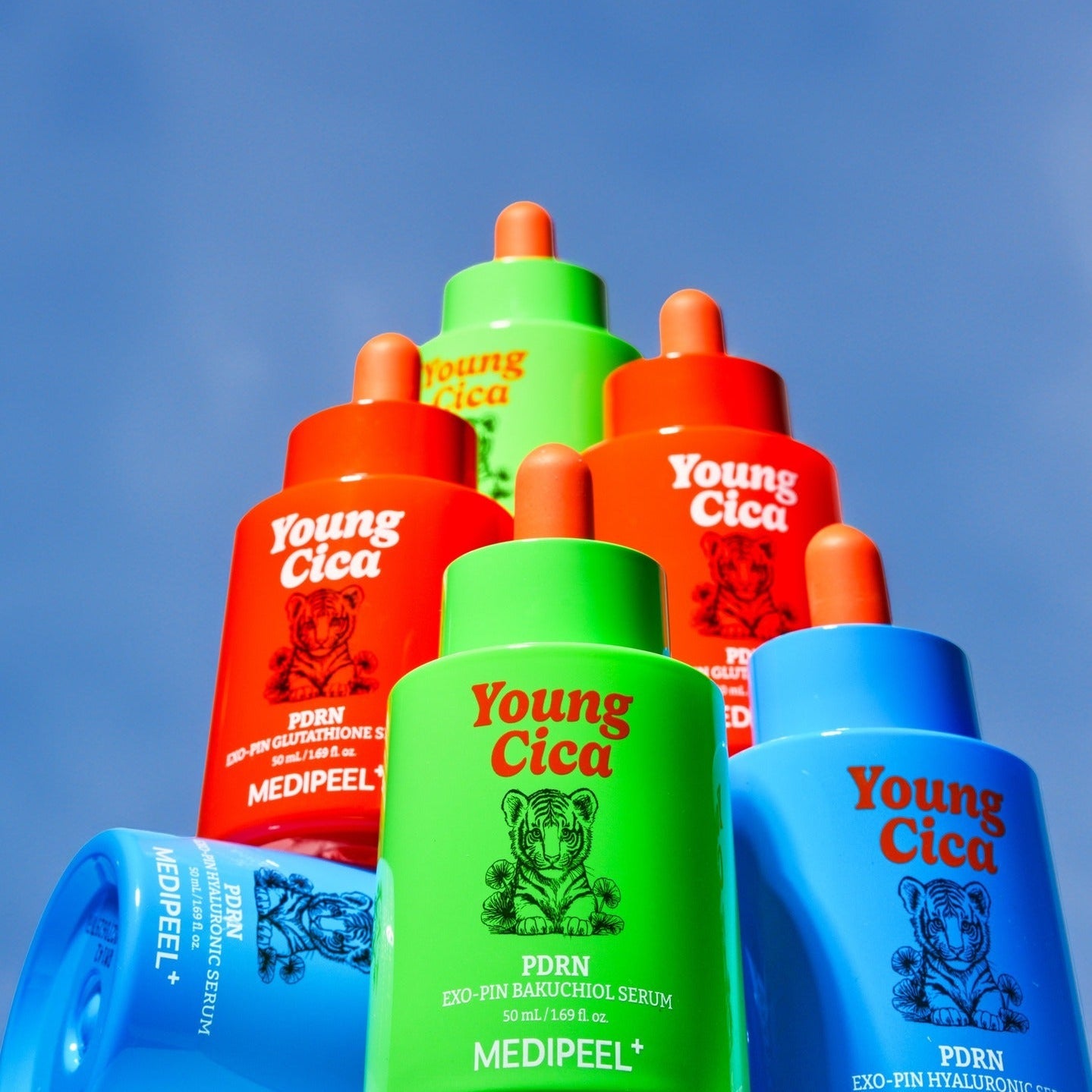 Five colorful bottles of MEDIPEEL Young Cica PDRNExo-Pin Hyaluronic Serum 50ml stacked against a clear blue sky.