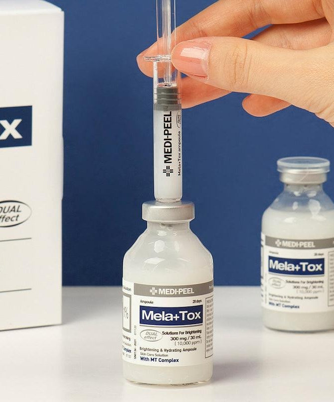 Hand holding syringe above MEDIPEEL Mela Plus Tox Ampoule 35ml with product displayed on table
