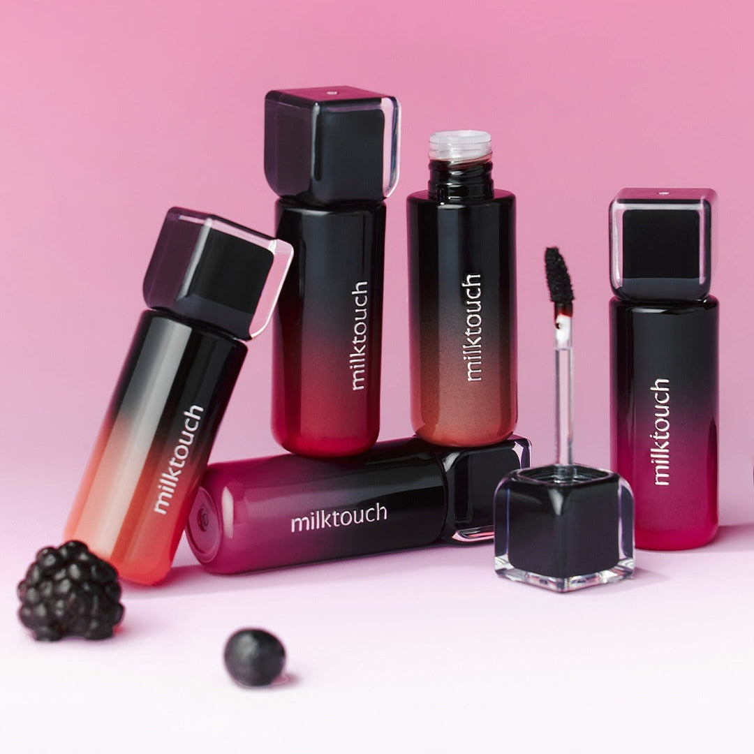 MILK TOUCH Black Peel-Off Lip Tattoo bottles and applicators displayed on a pink background with blackberries.