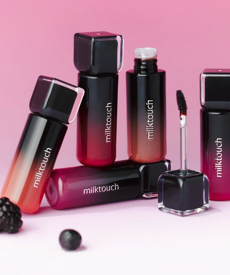 MILK TOUCH Black Peel-Off Lip Tattoo bottles and applicators displayed on a pink background with blackberries.