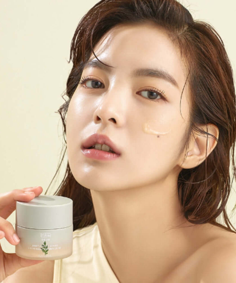 Model applying MISSHA Artemisia soothing cream 50ml on face, featuring product jar held in hand, highlighting skincare benefits.