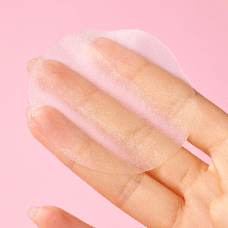 Close-up of a hand holding MIXSOON Collagen Toner Pad against a pink background, showcasing its texture and size.