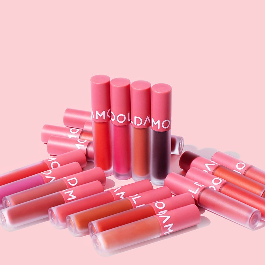 MOOLDA Tattoo Fixing Lip Tint collection in various shades of pink and red on a pink background.