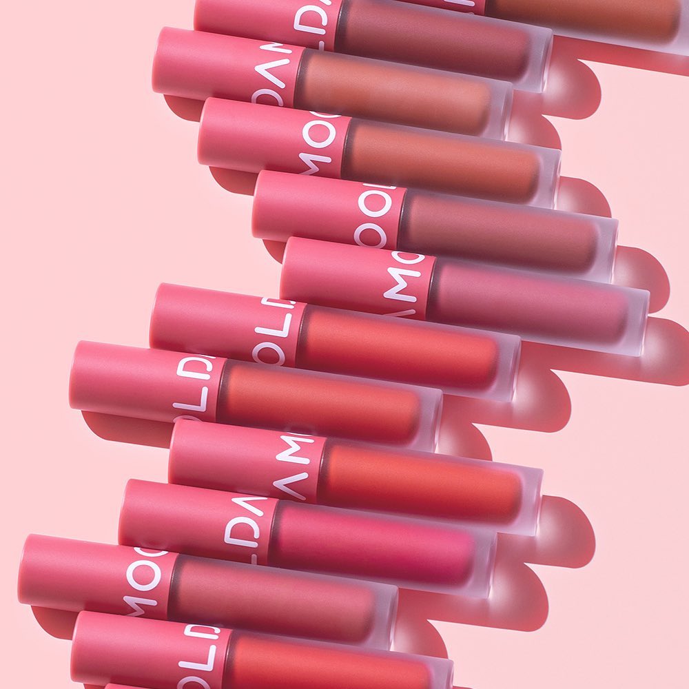 MOOLDA Tattoo Fixing Lip Tint collection in various shades displayed against a pink background, showcasing vibrant lip colors.