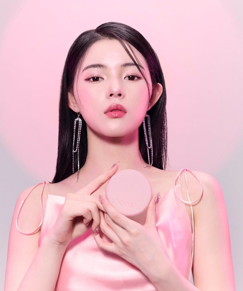 Model holding MOONSHOT Conscious Fit Cushion Foundation Pink Moon Edition in front of pink background, showcasing beauty and elegance.