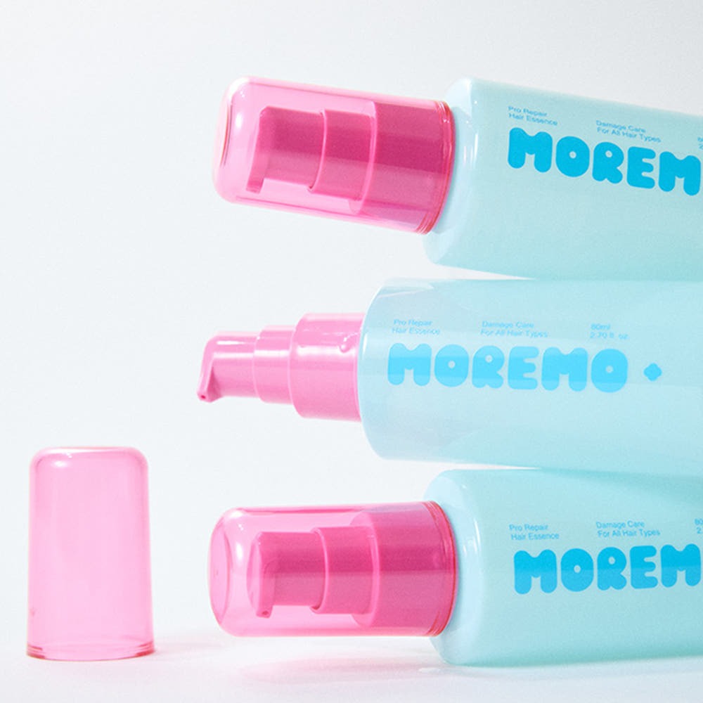 Three bottles of MOREMO Pro Repair Hair Essence with pink caps stacked on white background.