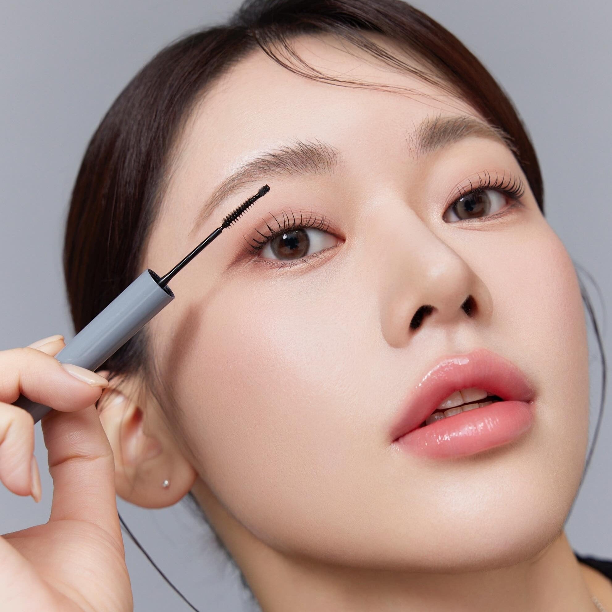 Close-up of a model applying mascara with precision, showcasing long lashes and smooth skin for beauty and makeup inspiration.