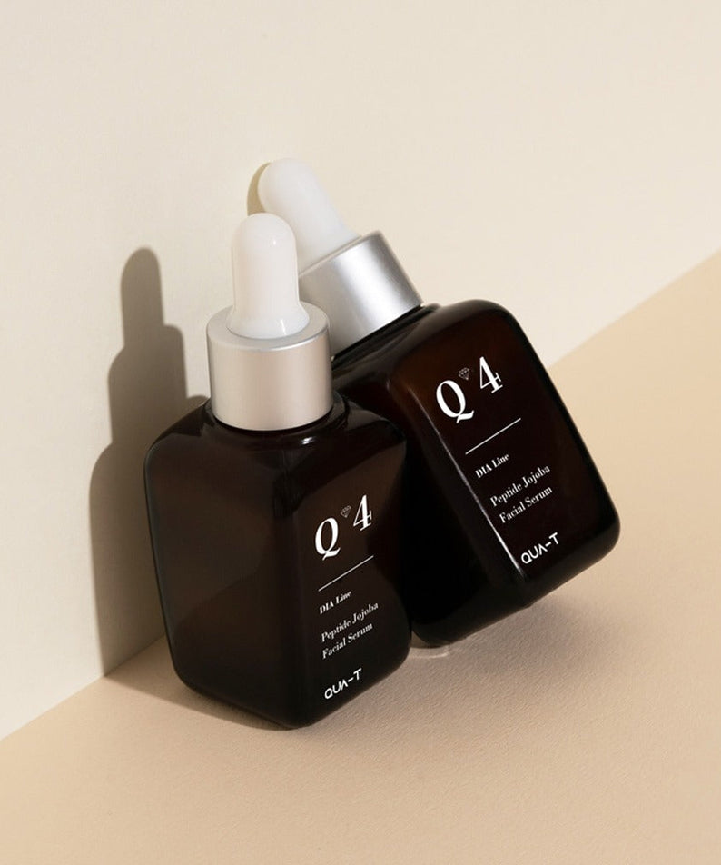 Two bottles of QUA-T Dia Peptide Jojoba Facial Serum 30ml on a beige surface