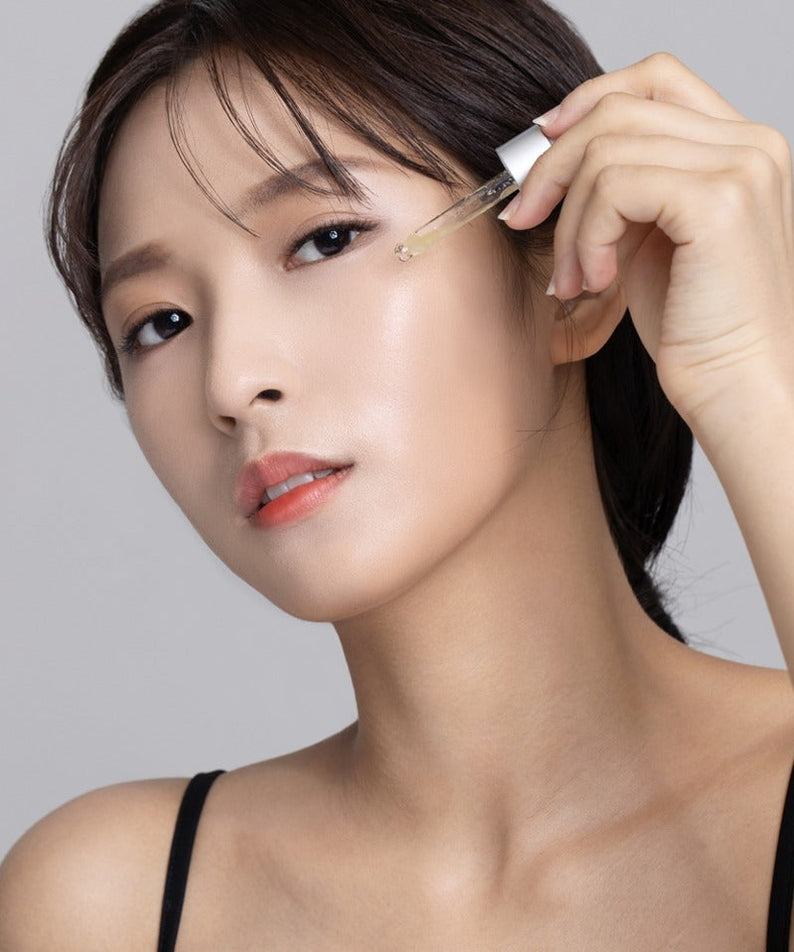 Woman applying QUA-T Dia Peptide Jojoba Facial Serum 30ml to her face for skincare.