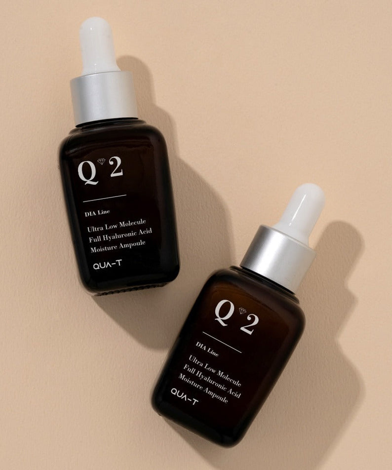 Two bottles of QUA-T Dia ultra-low molecular weight full hyaluronic acid moisture ampoule 30ml on a beige surface