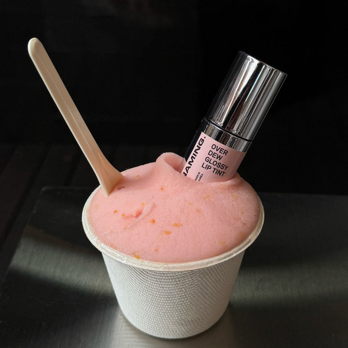 NAMING Overdew Glossy Lip Tint in pink dessert-like texture with spoon, showcasing shiny lip product.