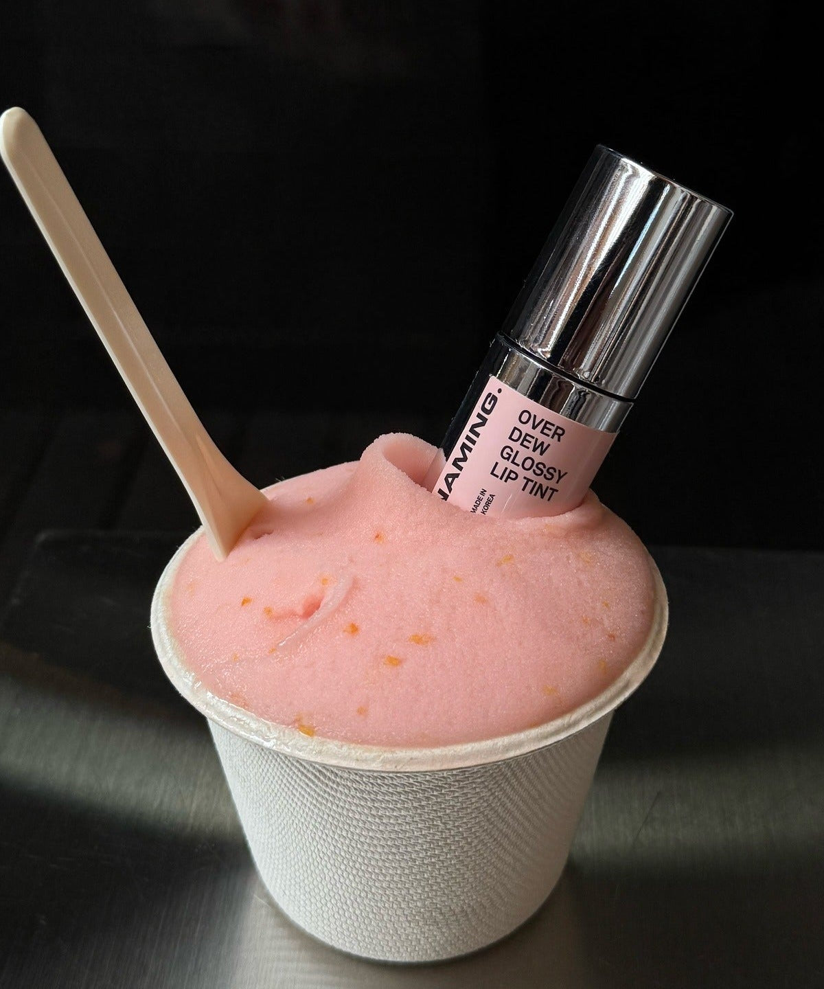 NAMING Overdew Glossy Lip Tint in pink dessert-like texture with spoon, showcasing shiny lip product.