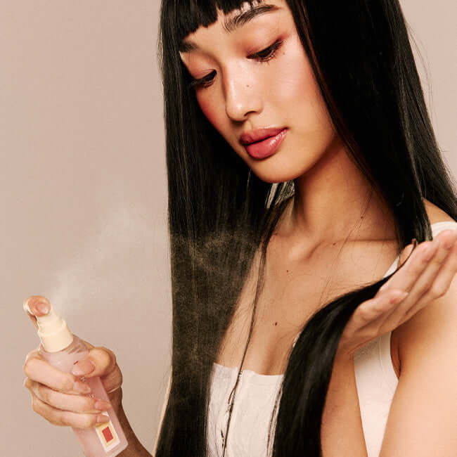 Woman applying NARKA Creamy Veil Hair Mist to long straight hair for a smooth and silky finish.