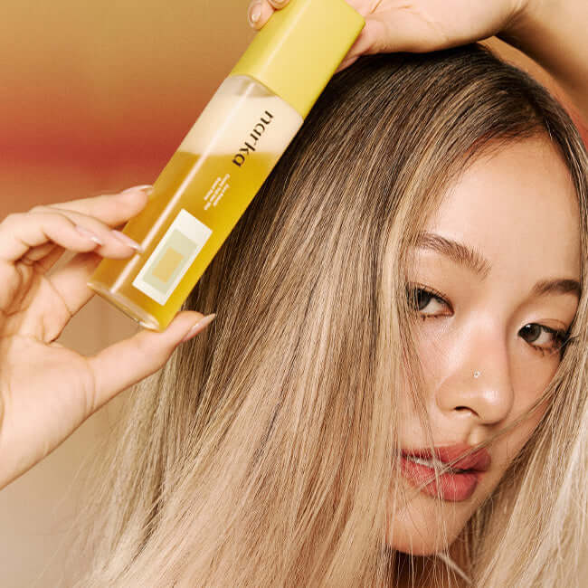 Person holding a bottle of NARKA Creamy Veil Hair Mist close to their hair, showcasing the product's packaging and use.