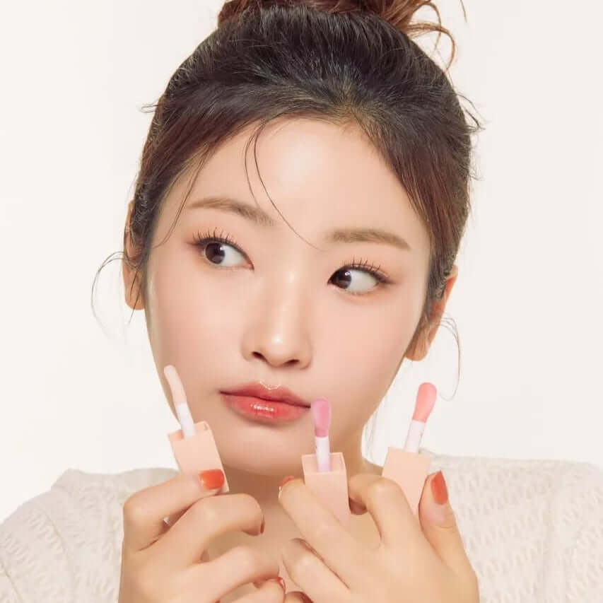 Woman holding NATURE REPUBLIC Glaze Shine Lip Oil with various shades, showcasing shiny lip finish.