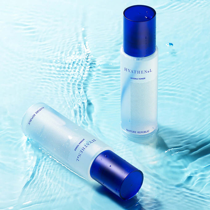 Two bottles of NATURE REPUBLIC Hyathenol Hydra Toner 150ml placed on a blue watery surface.