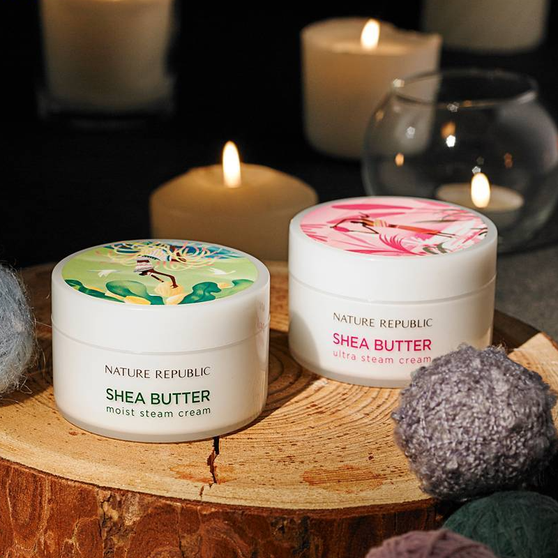 NATURE REPUBLIC Shea Butter Steam Cream 100ml placed on a wooden surface with candles in the background for a cozy ambiance.
