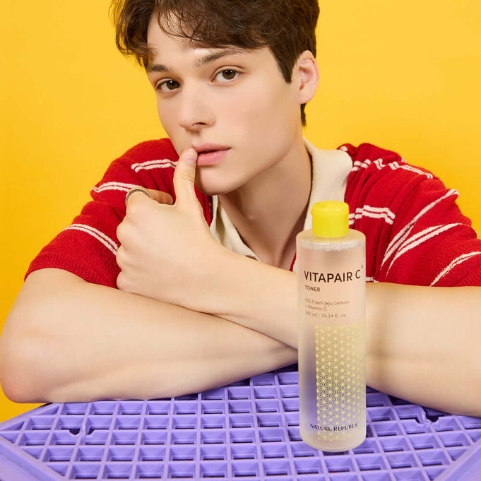 Person posing with NATURE REPUBLIC VitaPair C Toner 300ml against yellow background, highlighting the skincare product.