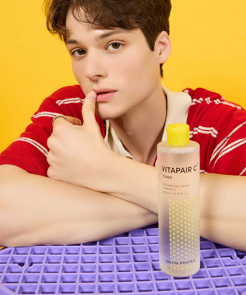 Person posing with NATURE REPUBLIC VitaPair C Toner 300ml against yellow background, highlighting the skincare product.