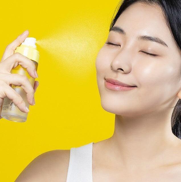 Woman using NATURE REPUBLIC Vitapair C Blending Serum Mist 80ml on her face against a yellow background.